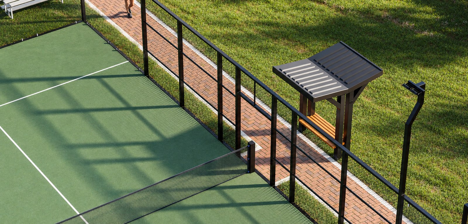 A courtside bench shade structure with a louvered roof and slat seat set on the paver walkway alongside a tennis court, beside the court fence and light pole.